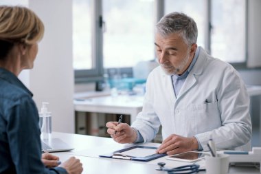 Doctor sitting at desk in his office and writing a medical prescription for his patient