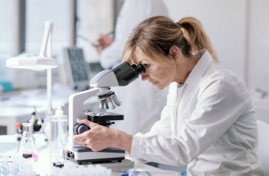 Woman working in a medical laboratory, she is using a microscope