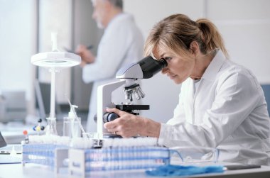 Woman working in a medical laboratory, she is using a microscope