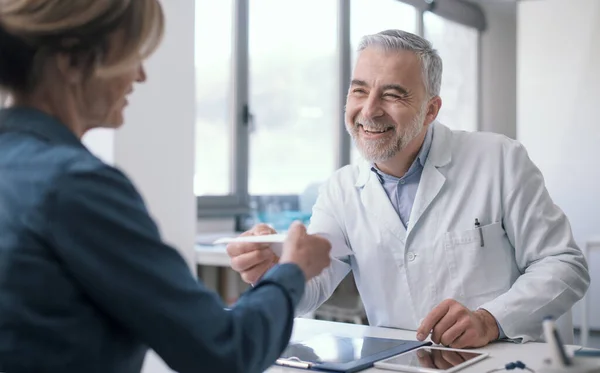 Χαμογελώντας Γιατρός Κάθεται Στο Γραφείο Και Δίνει Ιατρική Συνταγή Στον — Φωτογραφία Αρχείου