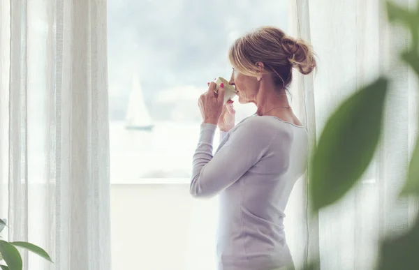 Mature Woman Relaxing Home Standing Next Window She Looking Away — Stok fotoğraf
