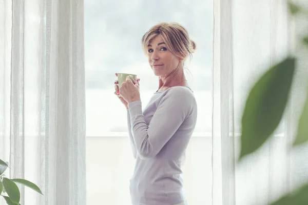 Mature Woman Relaxing Home Standing Next Window She Looking Away — Stock Fotó