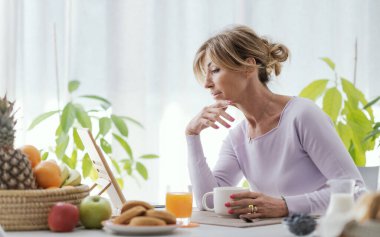 Mature woman having a relaxing breakfast at home, she is connecting online using her digital tablet