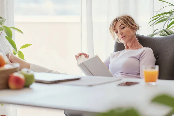 Mature Woman Sitting Feet Desk Reading Book — 图库照片