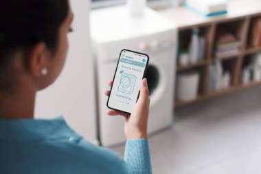 Woman connecting her smart washing machine to her phone and setting the washing program