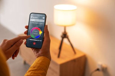 Woman controlling smart lighting at home, she is setting light color using her smartphone