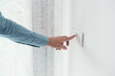 Woman pressing a light switch, energy saving concept