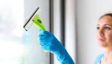 Woman washing windows at home, she is drying the glass surface with a squeegee
