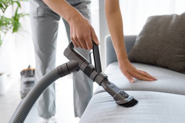 Young woman cleaning the couch in the living room, she is vacuuming the cushions using a vacuum cleaner
