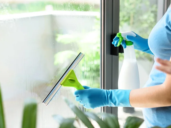 Woman washing windows at home, she is drying the glass surface with a squeegee