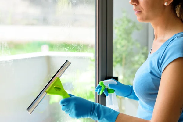 Woman washing windows at home, she is drying the glass surface with a squeegee