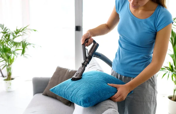 Young woman cleaning the couch in the living room, she is vacuuming the cushions using a vacuum cleaner