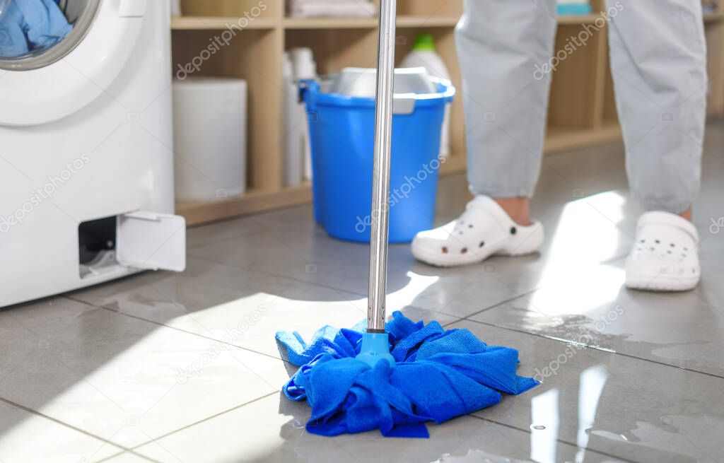Washing machine leaking and woman mopping, she is wiping the water on the floor