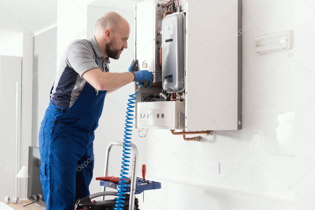 Gas engineer checking and cleaning a boiler during the inspection at home