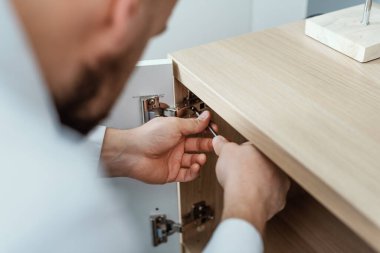 Man repairing a loose cabinet door hinge at home using a screwdriver