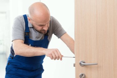 A professional repairman replaces a damaged lock, on an interior door.
