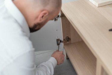 Man repairing a loose cabinet door hinge at home using a screwdriver