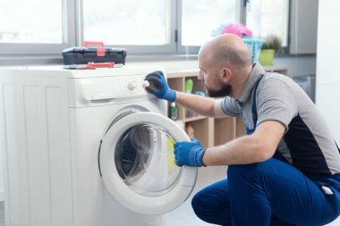 Professional technician checking a washing machine, he is adjusting a knob, home repair concept