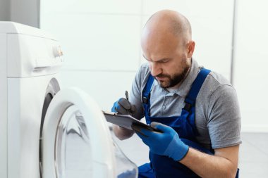 Professional technician writing an invoice after repairing a washing machine, home repair concept
