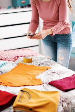 Woman taking pictures of her clothes on the bed, she wants to sell her second hand clothes online