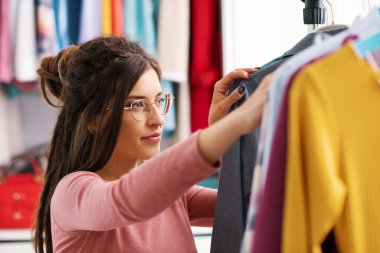 Young woman choosing clothes hanging on a rack, fashion and style concept