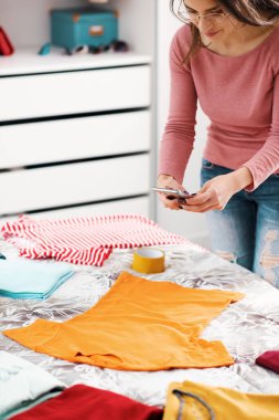 Woman taking pictures of her clothes on the bed, she wants to sell her second hand clothes online