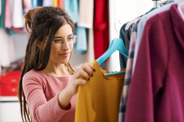 Young woman choosing clothes hanging on a rack, fashion and style concept