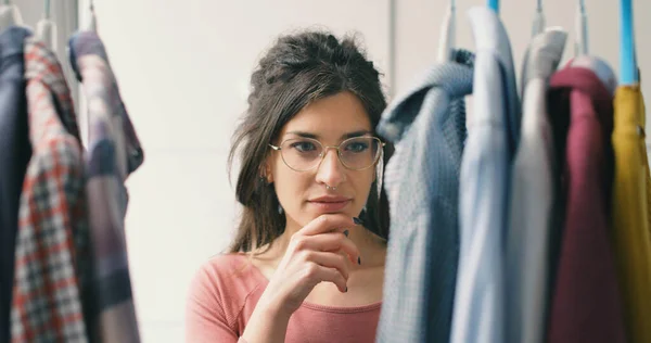 Young woman choosing clothes hanging on a rack, fashion and style concept