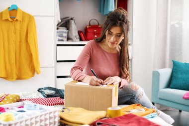 Woman preparing a delivery box with her used clothes, reselling and recycling concept