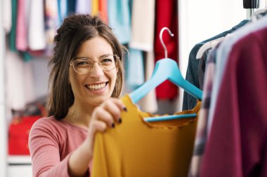 Young woman choosing clothes hanging on a rack, fashion and style concept