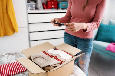 Young woman taking pictures of her clothes in a delivery box using a smartphone