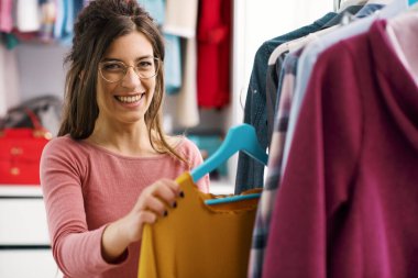 Young woman choosing clothes hanging on a rack, fashion and style concept