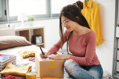Woman preparing a delivery box with her used clothes, reselling and recycling concept