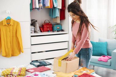 Woman preparing a delivery box with her used clothes, reselling and recycling concept