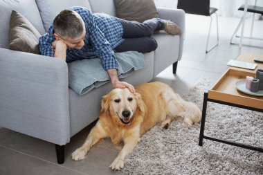 Man relaxing at home and cuddling his dog in the living room