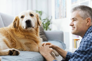 Cute happy dog and his owner posing in the living room at home, the man is holding his paws and the dog is looking at camera
