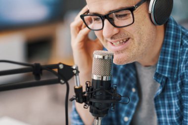 Smiling man wearing headphones and recording audio podcast using a professional microphone