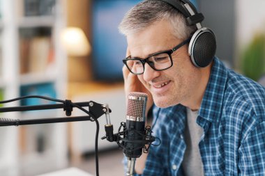 Smiling man wearing headphones and recording audio podcast using a professional microphone