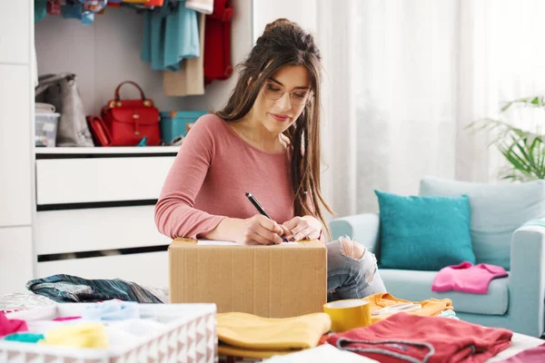 Woman preparing a delivery box with her used clothes, reselling and recycling concept