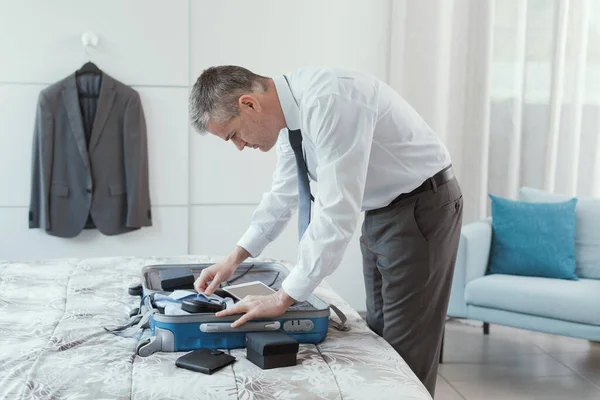 Corporate executive preparing for a business travel, he is packing his clothes and personal belongings in a trolley case