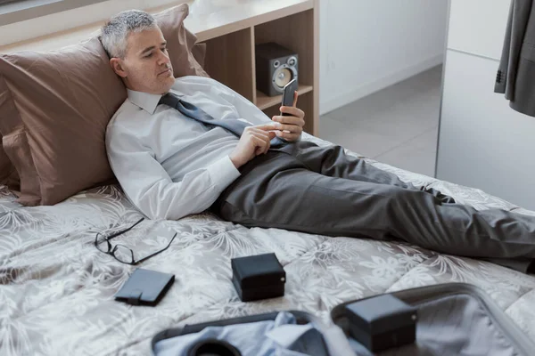 Businessman traveling for work, he is using his smartphone in the hotel room and searching online services