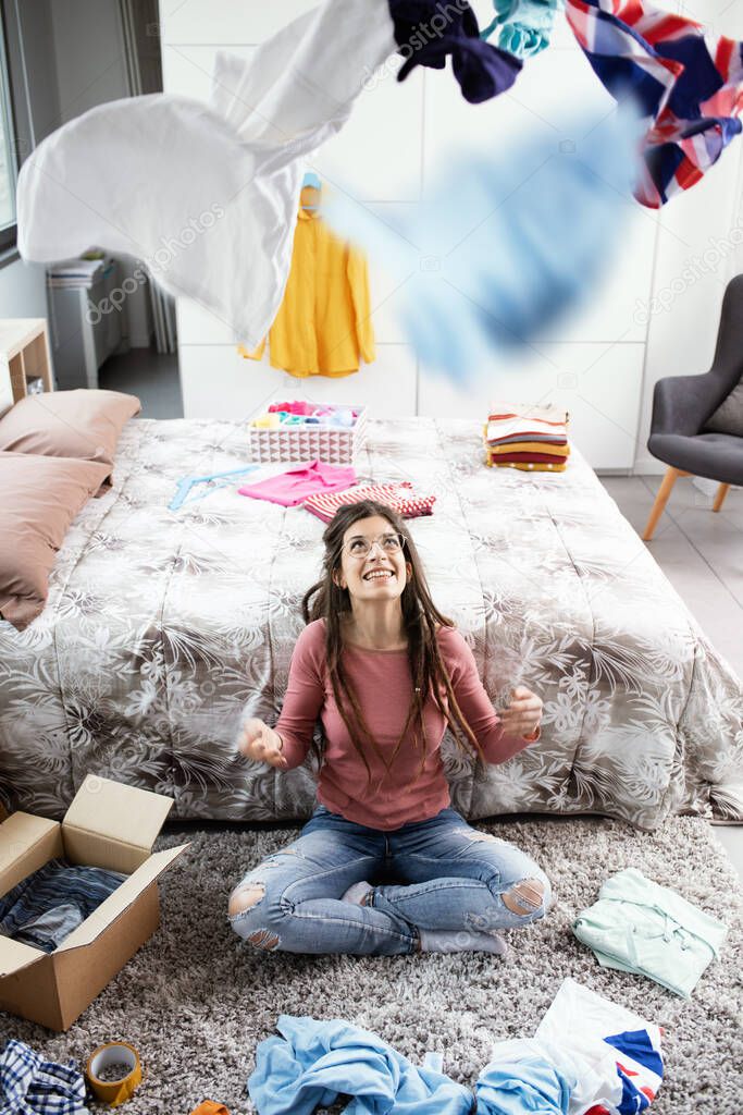 Young woman sitting on the floor in the bedroom and throwing clothes in air