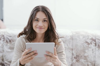Happy young woman relaxing at home and connecting online with her digital tablet, entertainment and technology concept