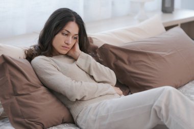 Sad young woman sitting on the bed at home, she is lonely and depressed