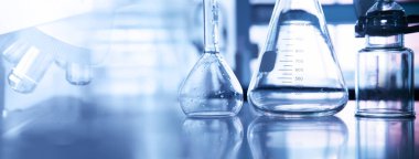 Kimya laboratuarında mikroskop ve bilimsel ekipman içeren konik ve hacimli cam şişe mor afiş arka planında 