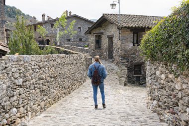 Güzel bir ortaçağ köyü caddesinde sırt çantasıyla yürüyen genç bir kadın. İspanyol Pirenelerinde geleneksel taş evleri ziyaret eden bir kadın.