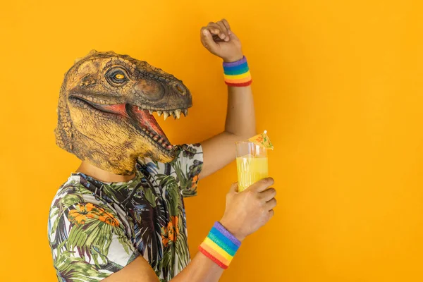 Man in dinosaur animal mask drinking cocktail and dancing wearing LGBTQ pride rainbow wristband,isolated on orange background