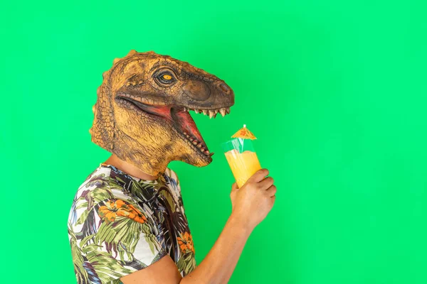 Man wearing dinosaur animal head mask drinking cocktail or fruits juice isolated on green background.