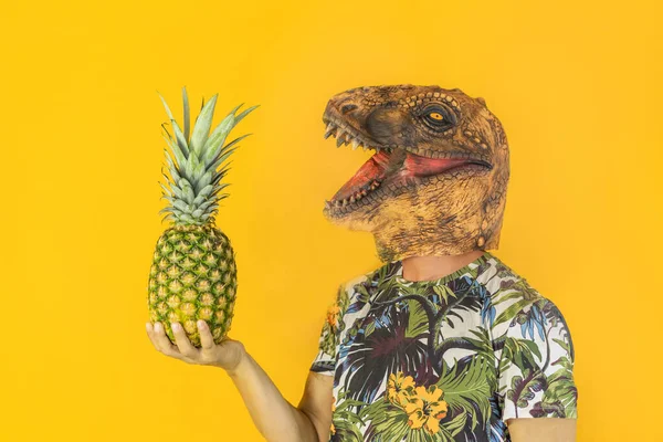 Man with dinosaur animal mask holding pineapple fruit isolated on yellow background.Copy space.Healthy food ,tropical concept.