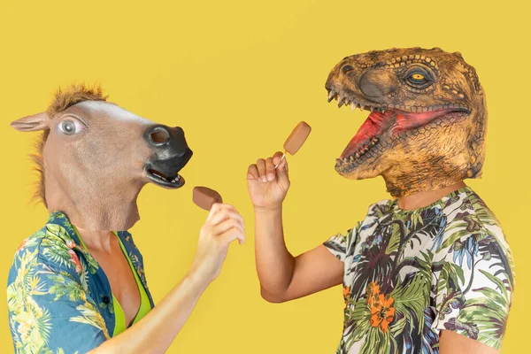 Man in dinosaur animal head mask and woman with horse head eating chocolate ice creams isolated on yellow background with copy space